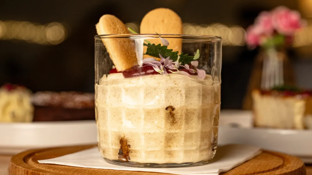 Poznańskie tiramisù o smaku rogala świętomarcińskiego – kremowy deser warstwowy z biszkoptami nasączonymi kawą, ozdobiony migdałami i lukrem, podany na talerzu w restauracji Just Friends na Starym Rynku w Poznaniu.