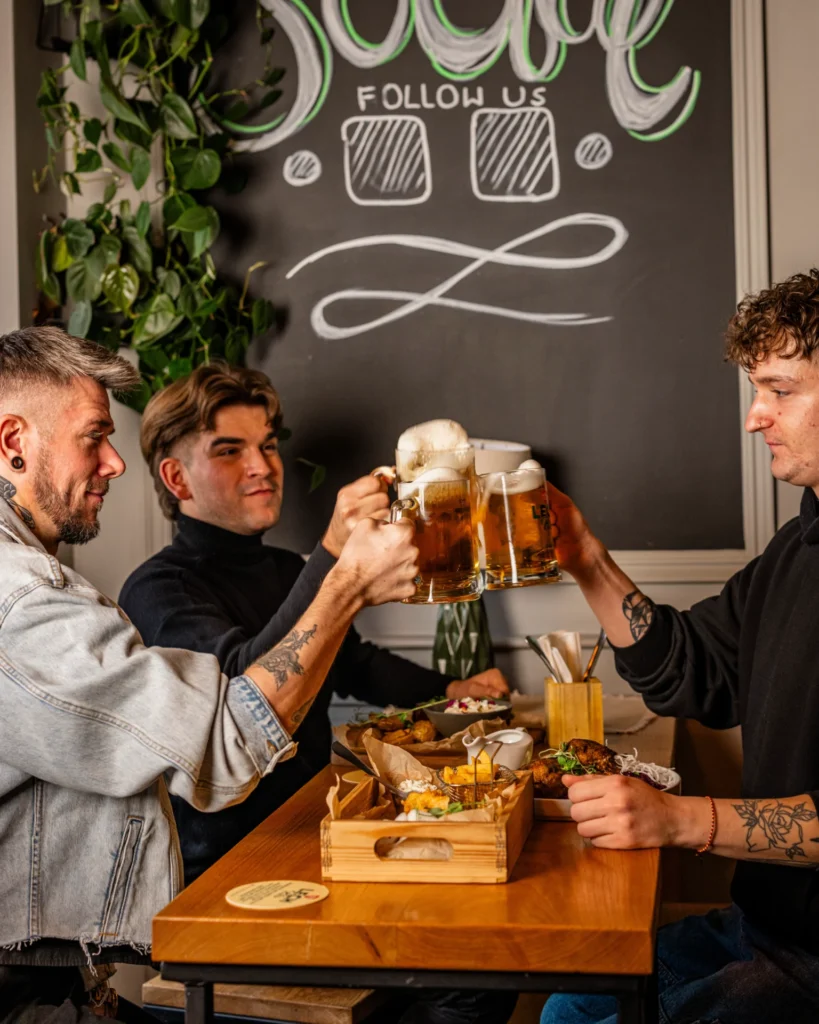 Grupa przyjaciół na kolacji integracyjnej w restauracji Just Friends w Poznaniu, wznosząca kieliszki do toastu przy stole z pysznymi daniami i piwem w tle.